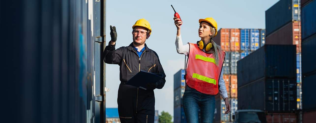 Logistics workers inspecting containers at shipping yard with radio and clipboard