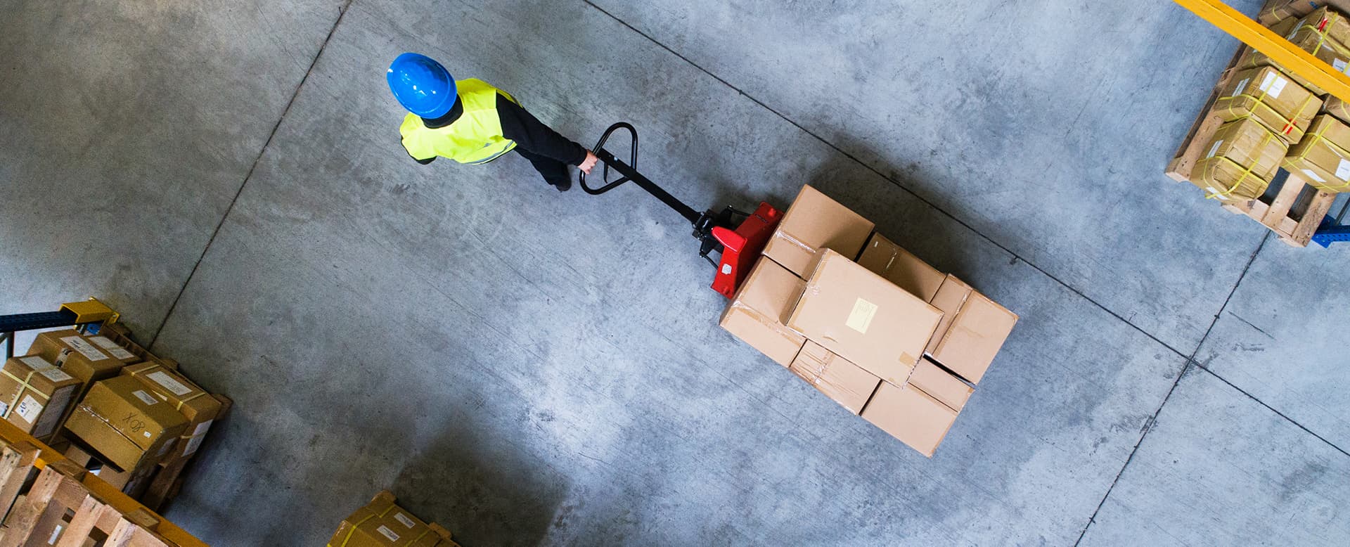 Warehouse worker pulling a pallet truck through a storage facility