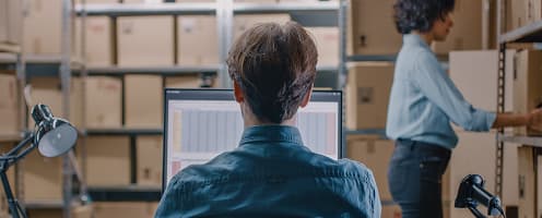 Warehouse staff managing inventory on computer with storage shelves in background