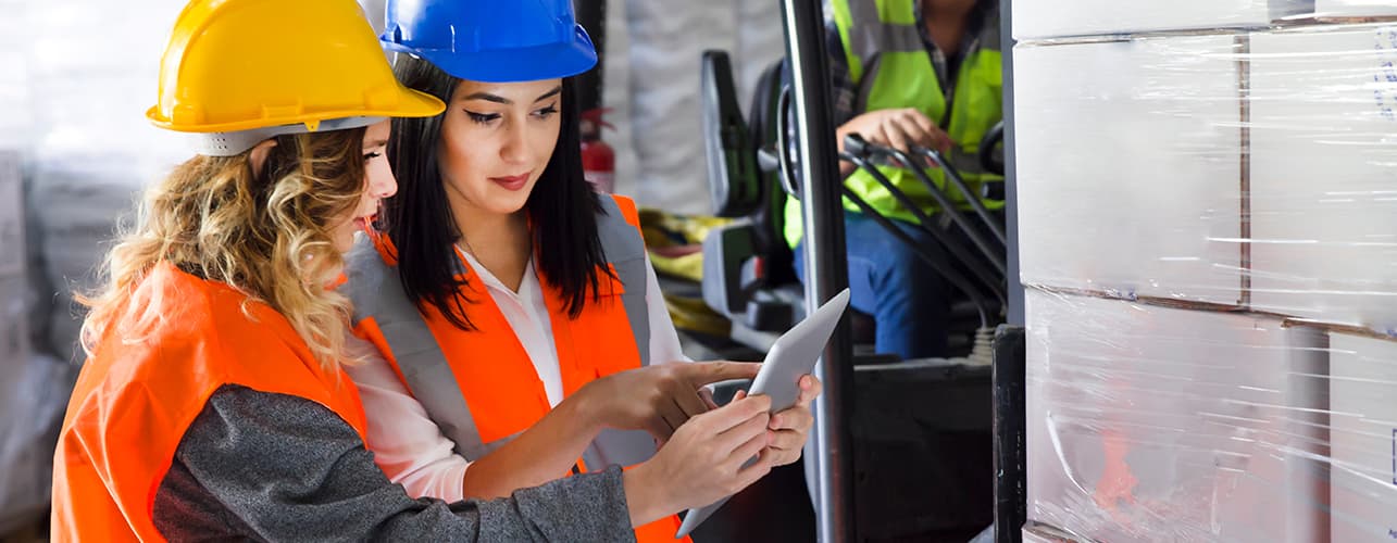 Women looking at tablet next to a forklift.