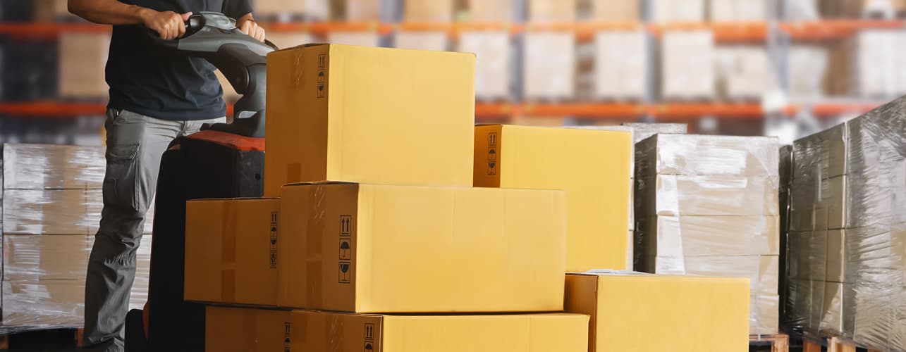 Warehouse worker transporting pallet of boxes with pallet jack